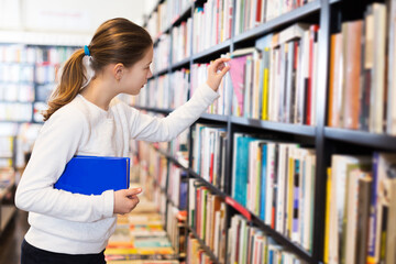 tweenager young girl searching for textbooks on bookshelves in store