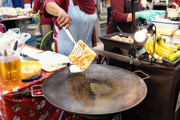 Thai woman is cooking banana pancake on pan with butter on the street.