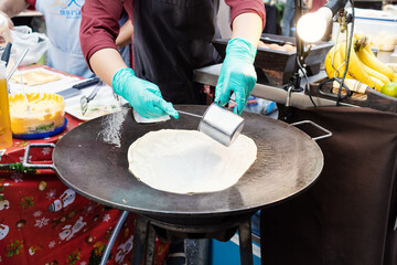 Thai woman is cooking banana pancake on pan with butter on the street.