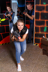 Obraz na płótnie Canvas Positive young girl with laser gun during lasertag game with players in labyrinth