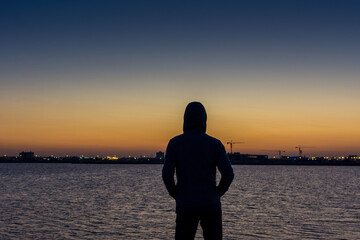 A man wearing jacket with hat watching sun rising from sea at the corniche park in Dammam, Kingdom Saudi Arabia