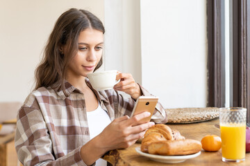 Woman viewing social networks using mobile, enjoying healthy breakfast. Concept for digital...