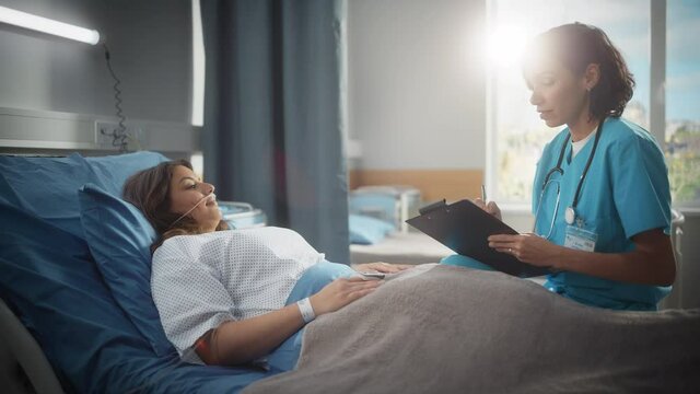 Hospital Ward: Friendly Hispanic Head Nurse Fills Medical History Form, Talks to Female Patient Recovering in Bed. Professional Nurse Helps Happy Woman Get Better after Surgery. Arc Side Slowmo Shot