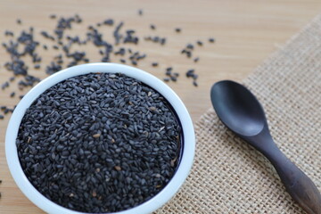 black sesame in the cup with wooden spoon on the wooden table.