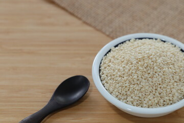White sesame in white cup with wooden spoon and wooden table top