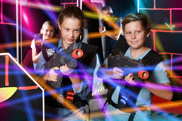 Positive girls and boys holding laser guns at other players during lasertag game with parents indoors..