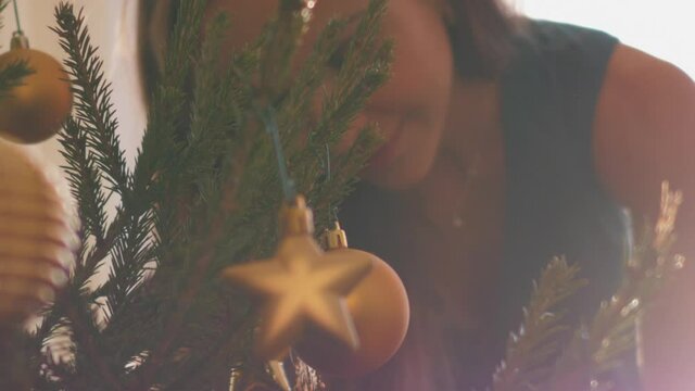 Golden star-shaped and round Christmas toys hang on thin green prickly Christmas tree twigs against young woman closeup. Concept holiday
