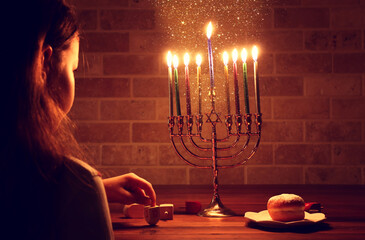 Low key image of jewish holiday Hanukkah background with girl looking at menorah (traditional...