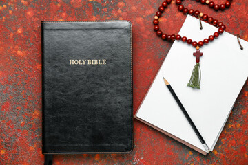 Hole Bible, notebook and rosary beads on color background