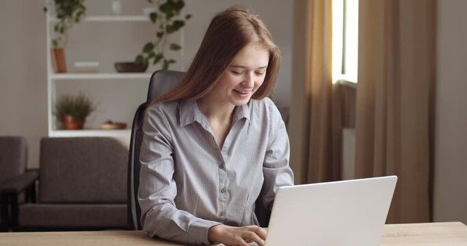 Young woman reads good news in laptop, rejoices, feels delight. Girl sitting at home or in office at table, typing on computer keyboard, checking mail, sending long-awaited letter, concept of success