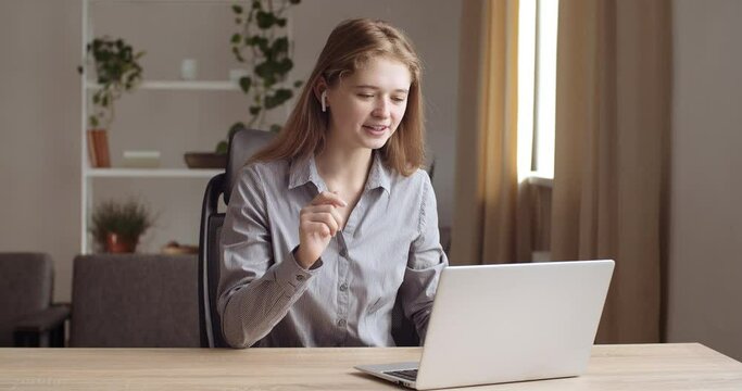 Portrait of female student sitting at home wears headphones speaks with teacher online through laptop web camera, studies on e-learning, speaks with friends actively gesticulates, shows with his hands