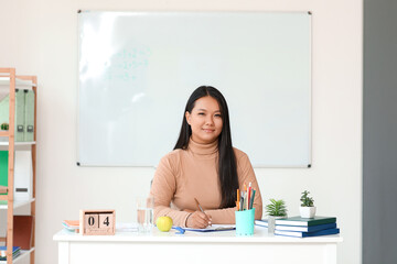 Asian female teacher sitting at table in classroom