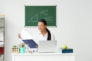 Asian female teacher sitting at table in classroom