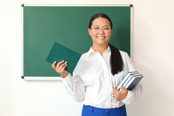 Asian female teacher near blackboard in classroom