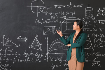 Asian female teacher near blackboard in classroom