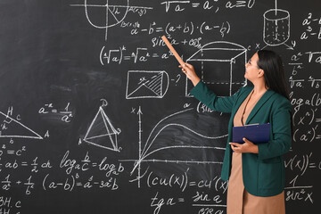 Asian female teacher near blackboard in classroom