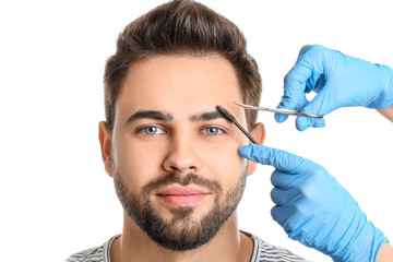 Young man undergoing eyebrow correction procedure on white background