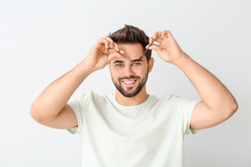 Naklejka premium Young man correcting eyebrows on light background