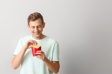 Young man with french fries on light background