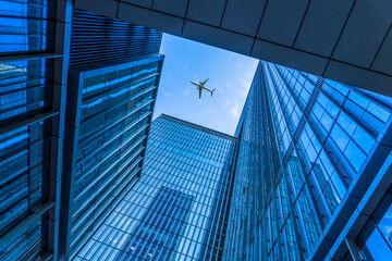 Tall city buildings and a plane flying overhead. - Powered by Adobe