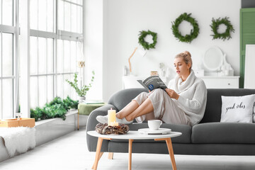 Beautiful young woman in warm sweater reading magazine at home