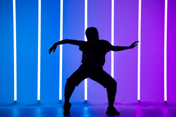 Young woman dancing street dance hip hop in a studio with neon lighting tube on a blue purple background. Dark silhouette. Dance and music poster design.