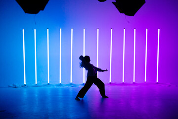 Attractive young woman dancer dancing contemporary in the studio on a blue purple background with neon lighting lamp.