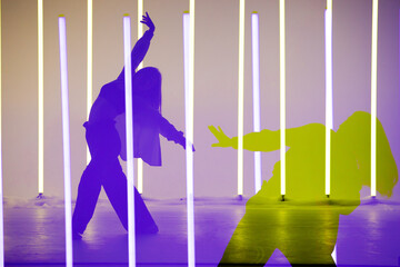 Collage of shadows trendy young woman dancing single in the studio on a colorful background with neon lighting tube.