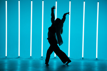 Pretty young woman dancer in a youth fashion streetwear dancing contemporary in the studio on a colorful background with neon lighting tube in disco style. Dance color poster.