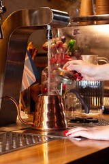 Barista in a coffee shop pours tap water into a copper kettle