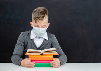 Teen schoolboy wearing mask reads a books at school near blackboatd during corona virus and flu outbreak. Empty space for text