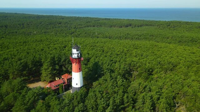 Aerial orbit around Stilo lighthouse in thick forest trees on Baltic Sea in Poland