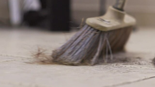 Close up on broom sweeping at hair salon, with hair cuttings fly in the air, slow motion low view