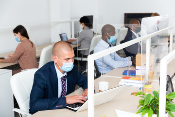 Typical working day in office of an IT company - programmers in protective mask work at a laptop