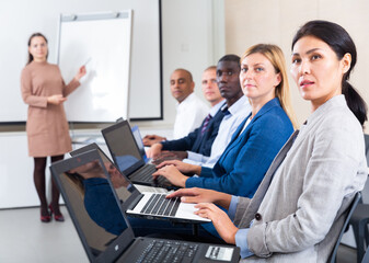 Fototapeta premium Portrait of concentrated Asian businesswoman sitting with her colleagues in conference room during corporate seminar, working on laptop