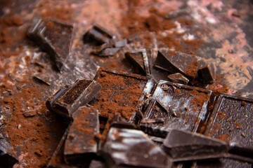 Dark chocolate bar with chocolate pieces with cocoa powder on brown background, close-up view
