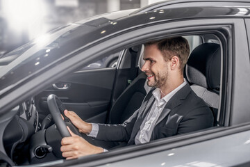 Fototapeta na wymiar Smiling young male sitting in car, holding steering wheel