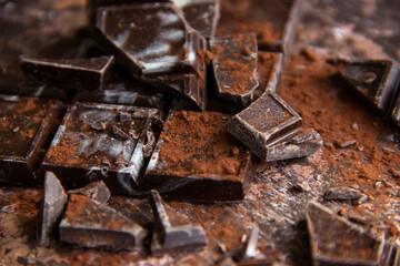 Dark chocolate bar with chocolate pieces with cocoa powder on brown background, close-up view