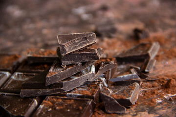 Dark chocolate bar with chocolate pieces with cocoa powder on brown background, close-up view