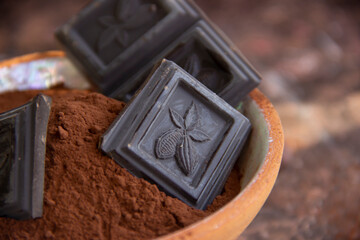 Bitter chocolate in a clay cup with cocoa on a blurred background, close-up view