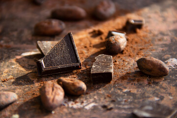 Pieces of dark chocolate with cocoa beans and cocoa butter on a brown background close up