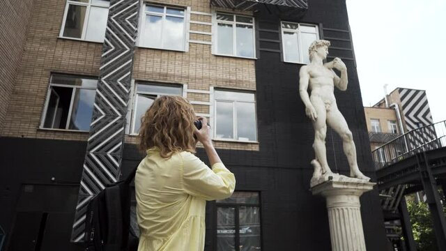 Pretty female tourist taking pictures of architectural elements in a city. Action. Woman with a professional camera photographing beautiful sculpture.