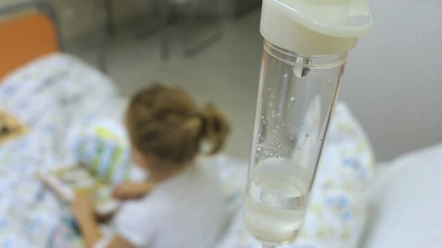 Young Girl on a Drip with Peripheral Venous Catheter Reading Book in Hospital