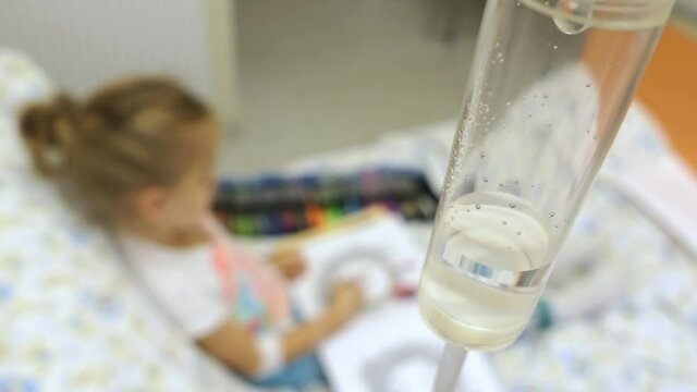 Young Girl on a Drip with Peripheral Venous Catheter Reading Book in Hospital