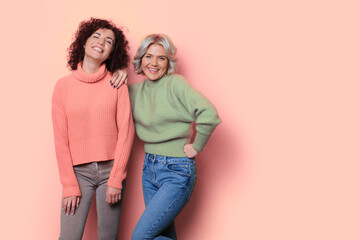 Monochrome photo of two women with curly hair posing on a studio wall with free space smiling at...