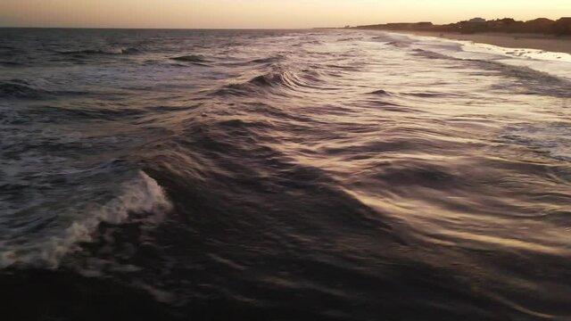 Fast drone shot at beach during warm sunset of waves rolling in.