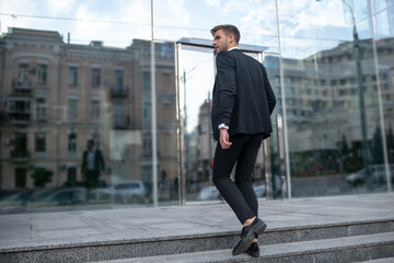 Elegant young man in a black suit on the steps outside