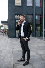 Young man in a black suit talking on the phone near business center