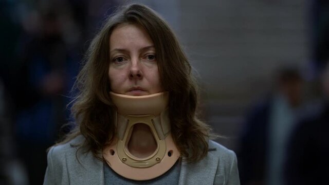 tired woman with osteochondrosis and neck ache is wearing cervical collar, standing on street in big city