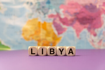 The word Libya written with wooden dices in front of a purple background and a geographic map